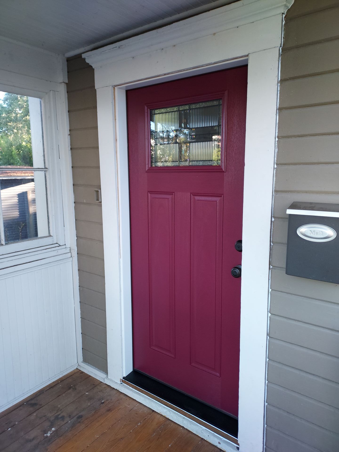 A red door is on the side of a house next to a mailbox.