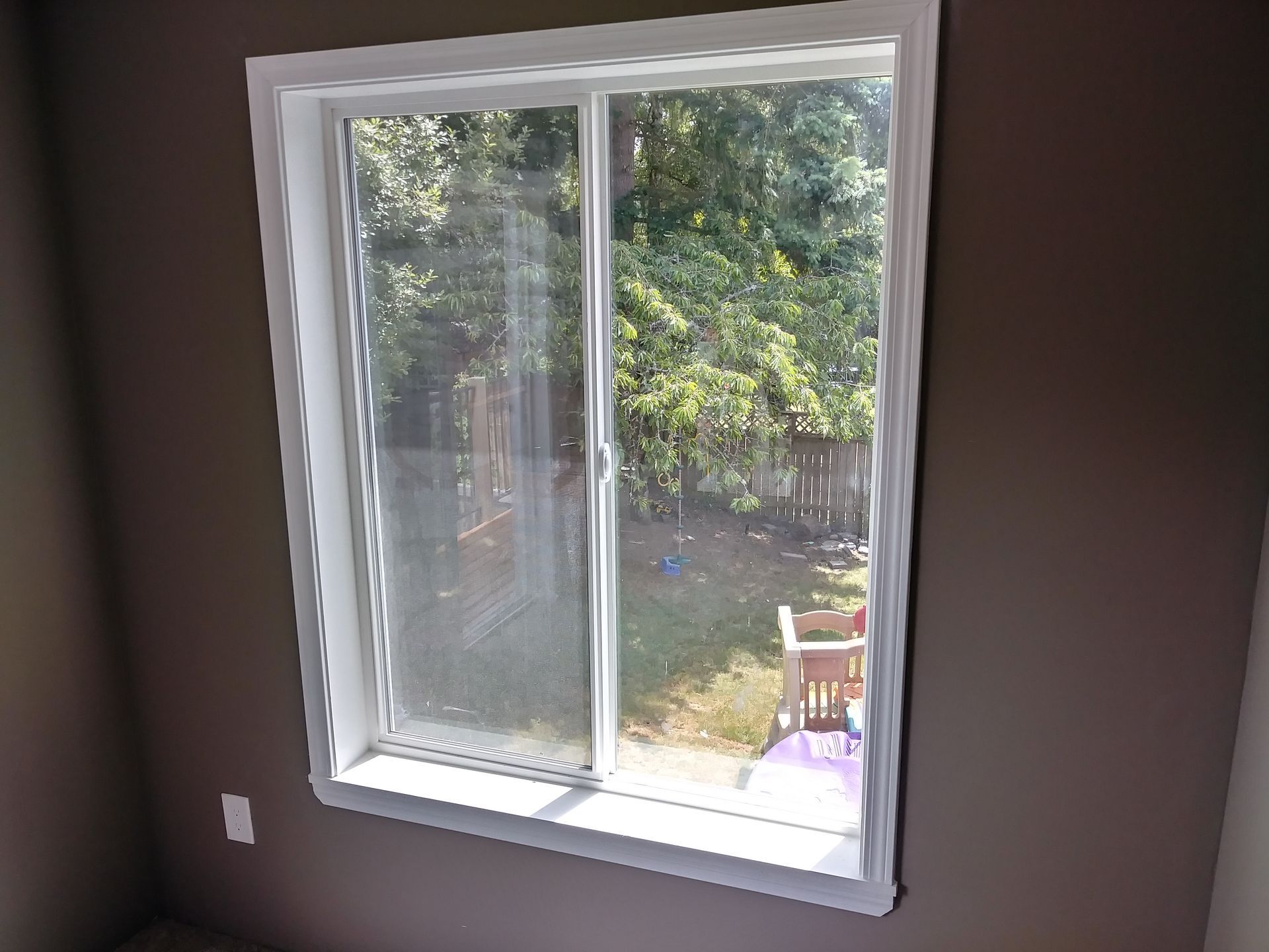 A window with a sliding glass door in a room with a view of a backyard.
