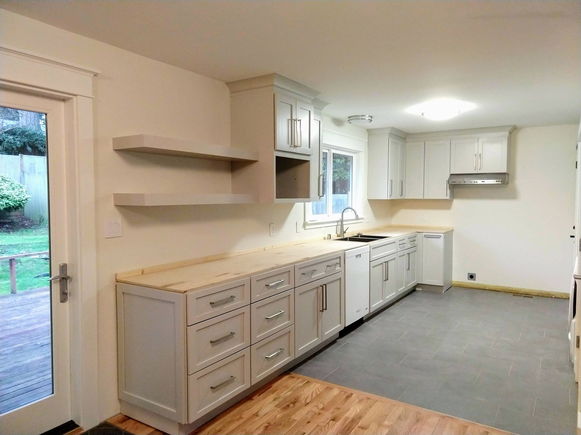 A kitchen with white cabinets , a sink , and a sliding glass door.