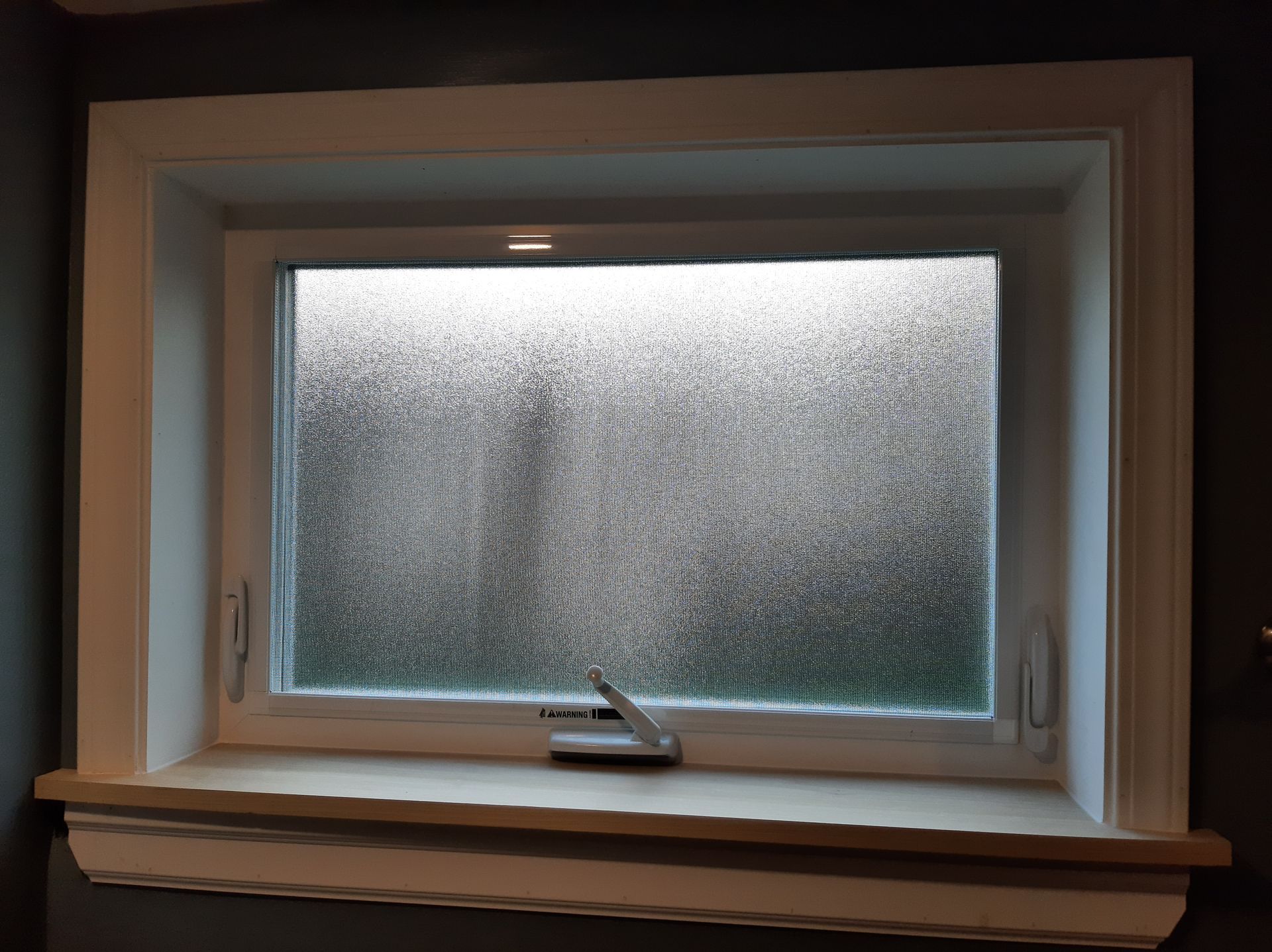 A window with a frosted glass covering is sitting on a window sill.