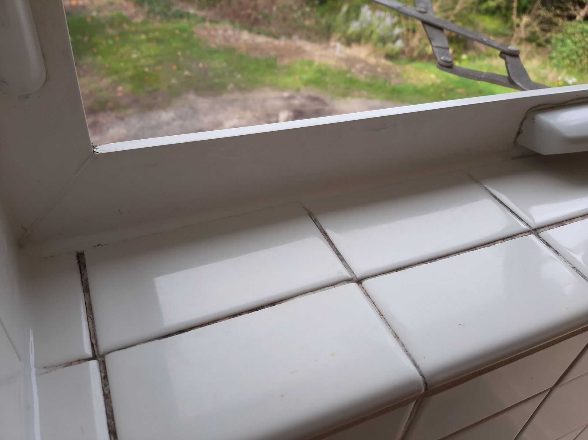 A window sill with white tiles and a view of a garden.