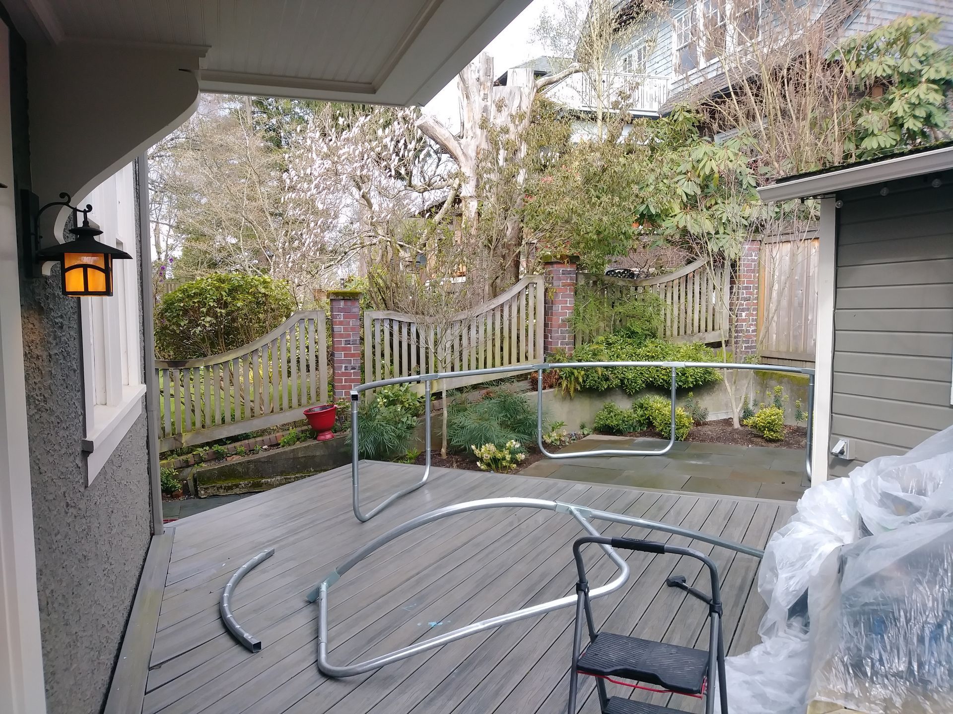 A trampoline frame is sitting on a wooden deck in front of a house.