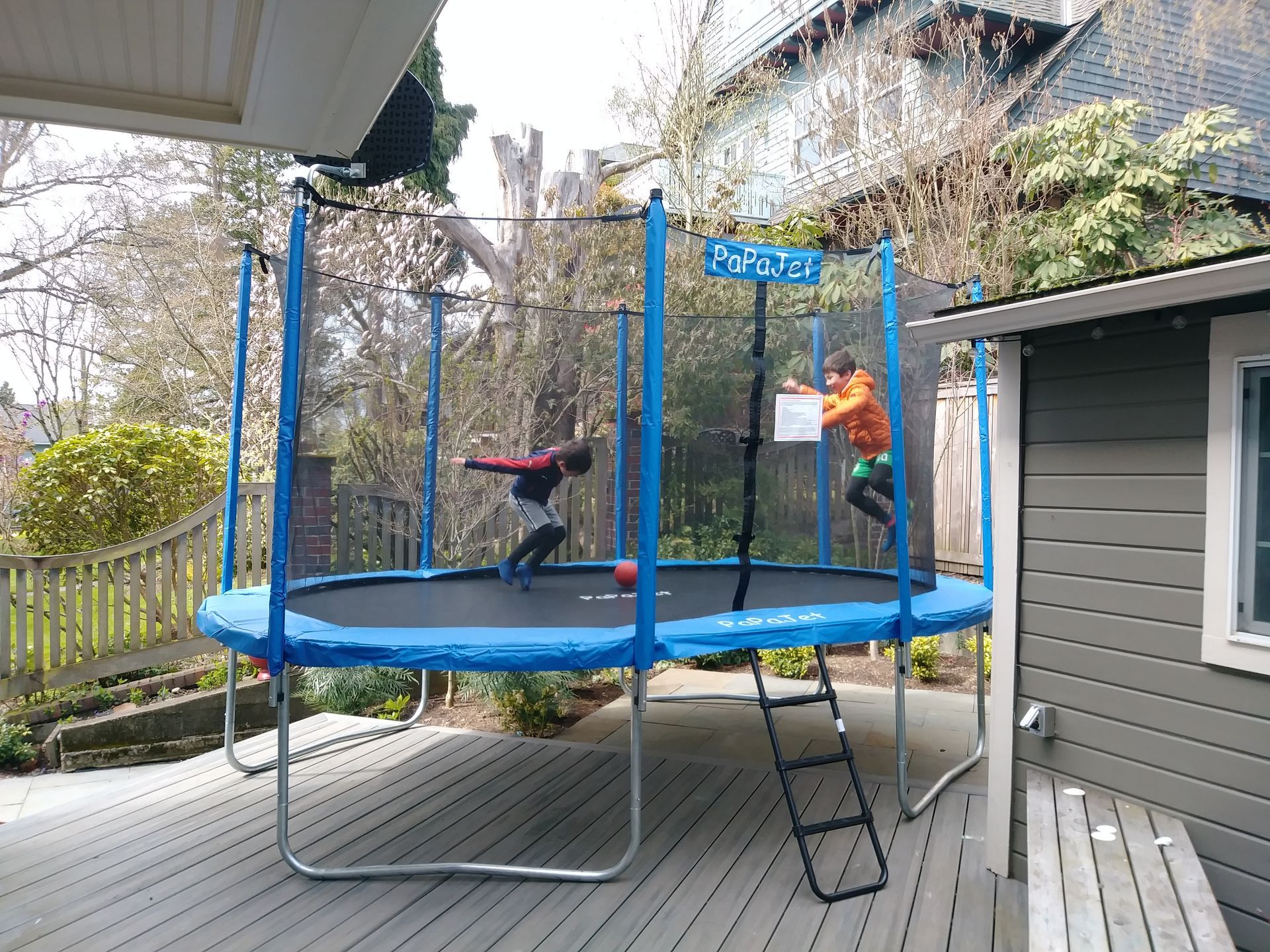 Two children are playing on a trampoline on a deck.