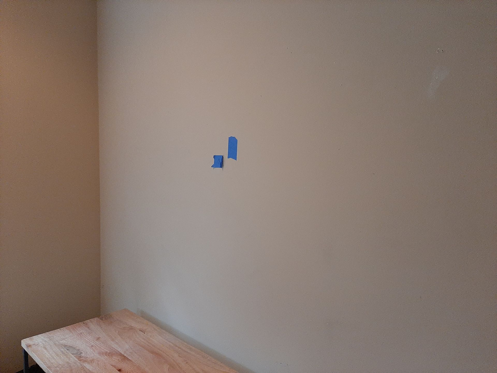 A room with a wooden table and a wall with blue tape on it.