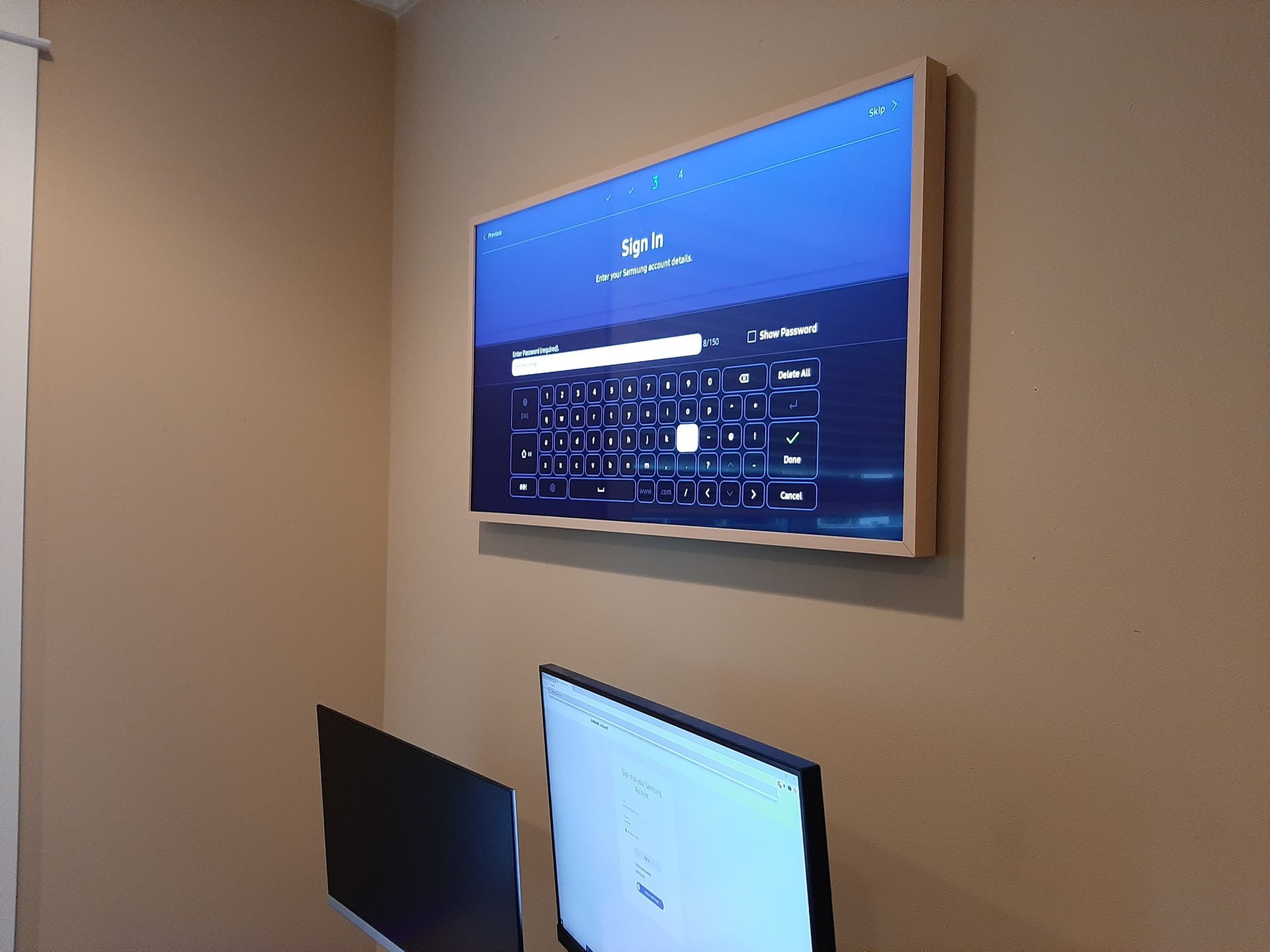 A flat screen tv is hanging on a wall next to two computer monitors.