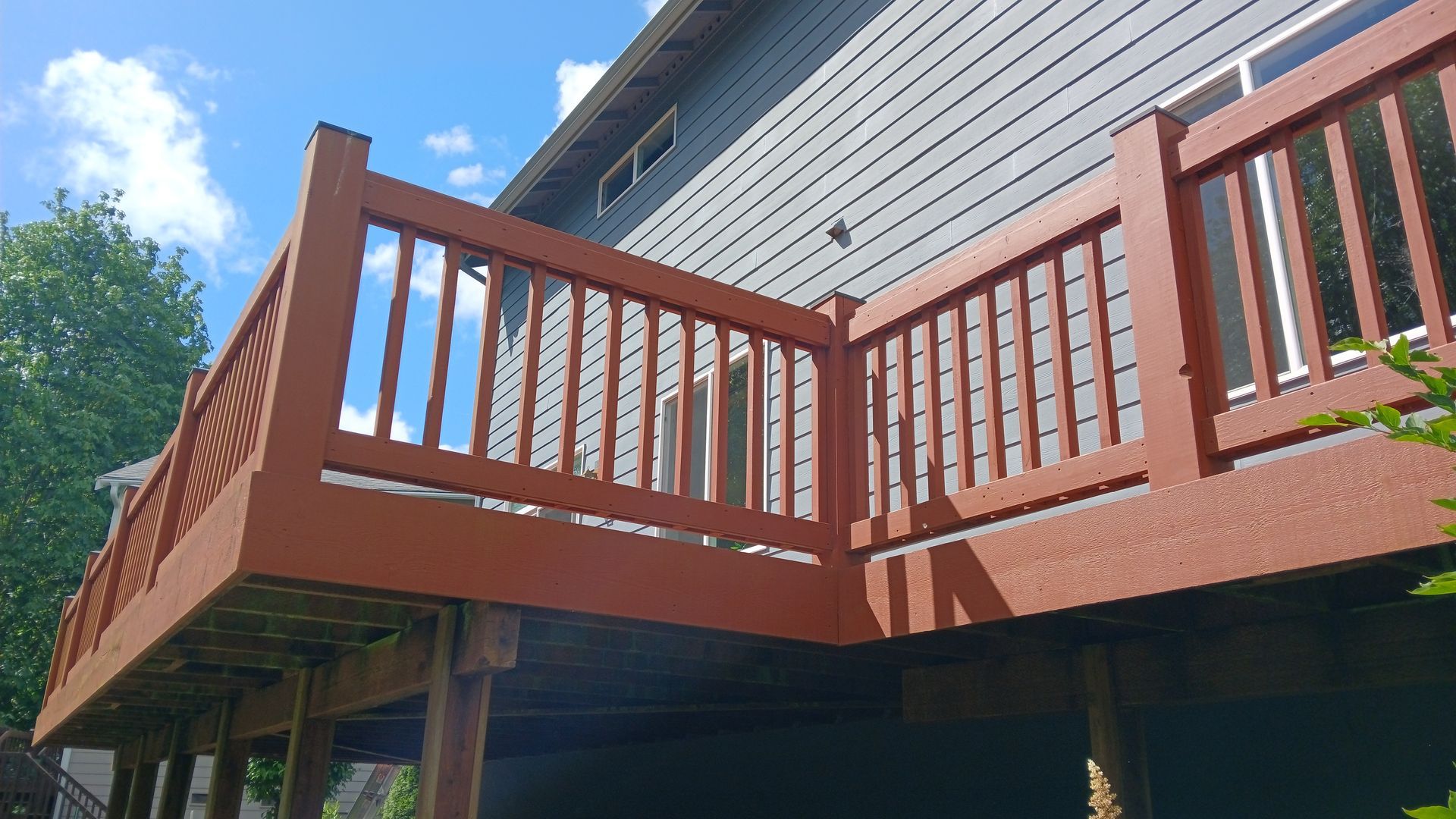 A wooden deck with a red railing is sitting on the side of a house.