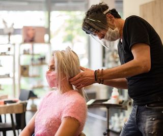 Keep-it-safe concept - Hairdresser with a face mask and a visor taking care of a client wearing a reusable fashionable Face mask