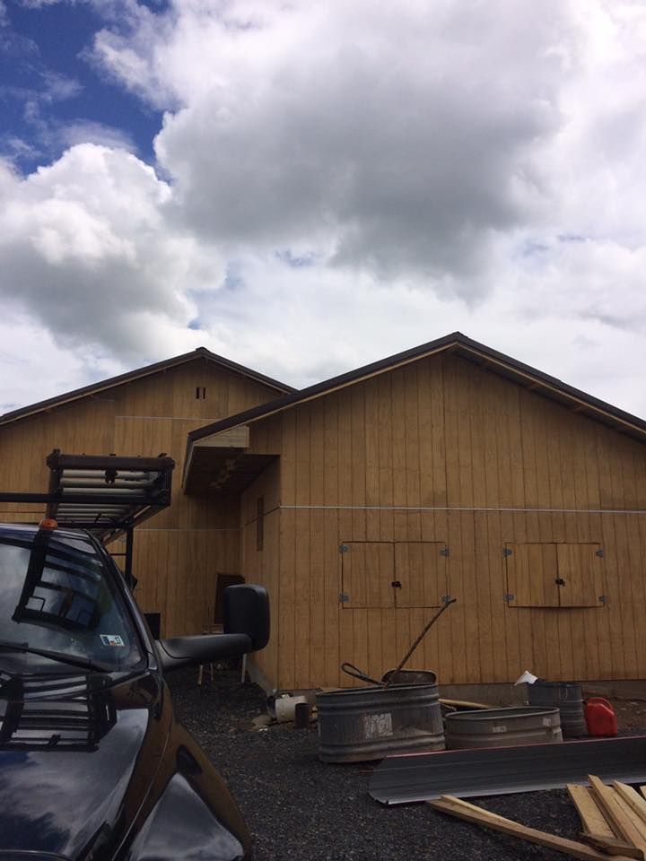 Wooden building under construction with dark accents, blue sky, and clouds.