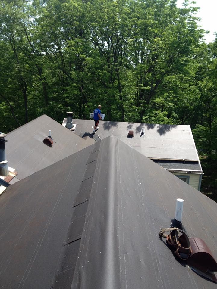 Person on dark roof, surrounded by trees, appearing to be working on the roof.