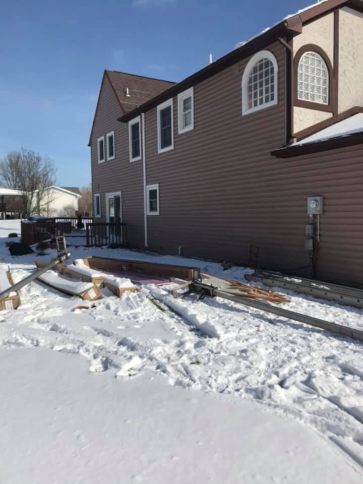 Snowy backyard with building materials and a brown two-story house with arched windows.