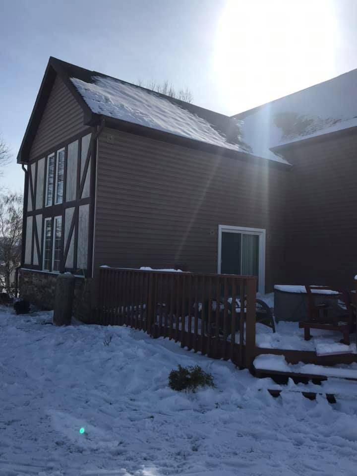 Snowy exterior of a brown house with a deck. The sun shines brightly.