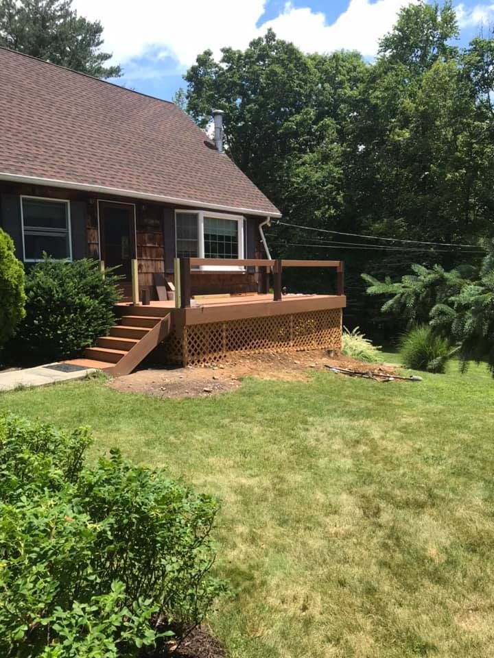 Brown house with wooden deck and stairs, set in a grassy yard.