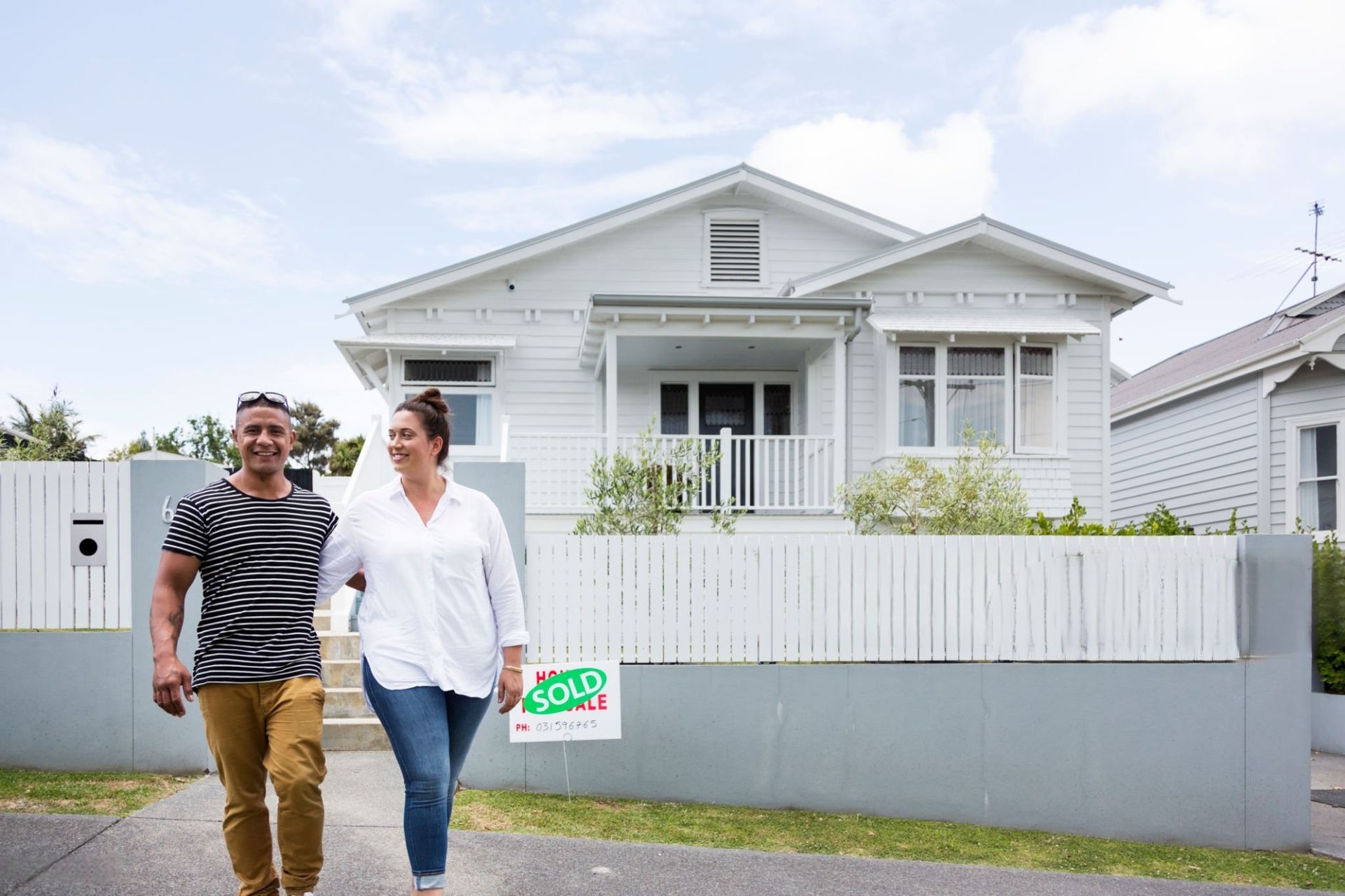 Couple walking arm in arm in front of a white house with a