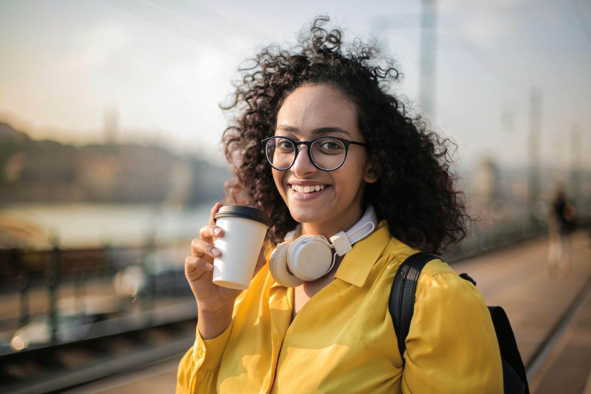 A woman in a yellow shirt is holding a cup of coffee.