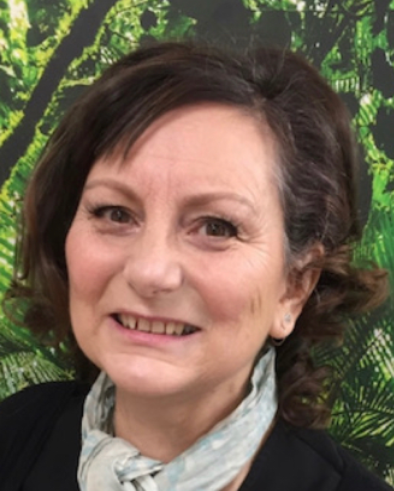 Portrait of a smiling woman with dark hair, wearing a scarf, against a leafy green background