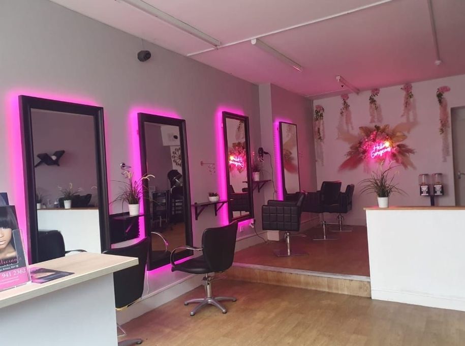 Modern salon interior with pink neon-lit mirrors, styling chairs, and glossy wood flooring