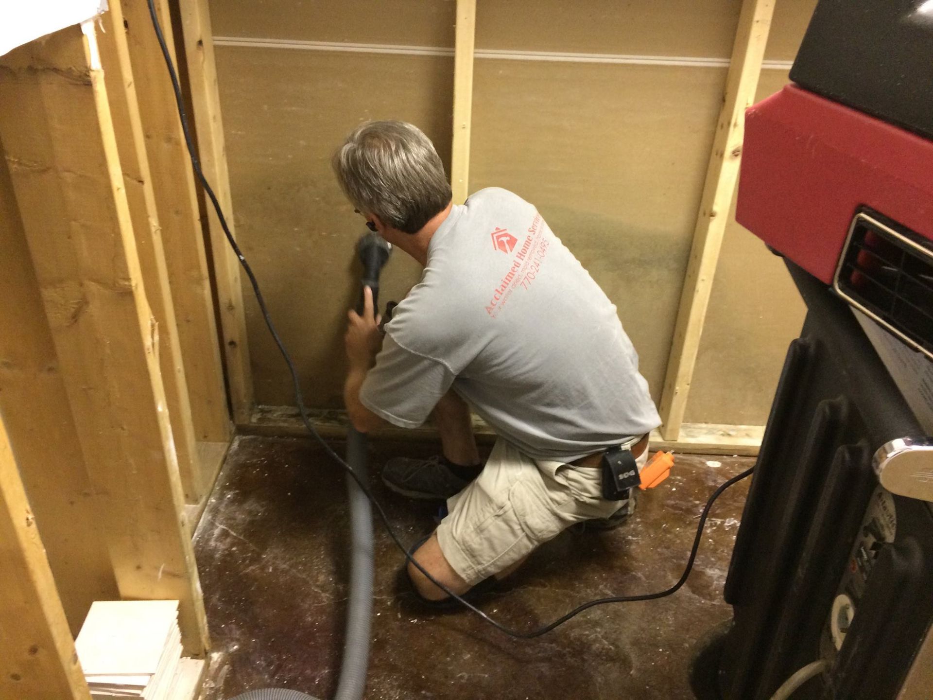 A man in a gray shirt cuts into a wall in a confined space.