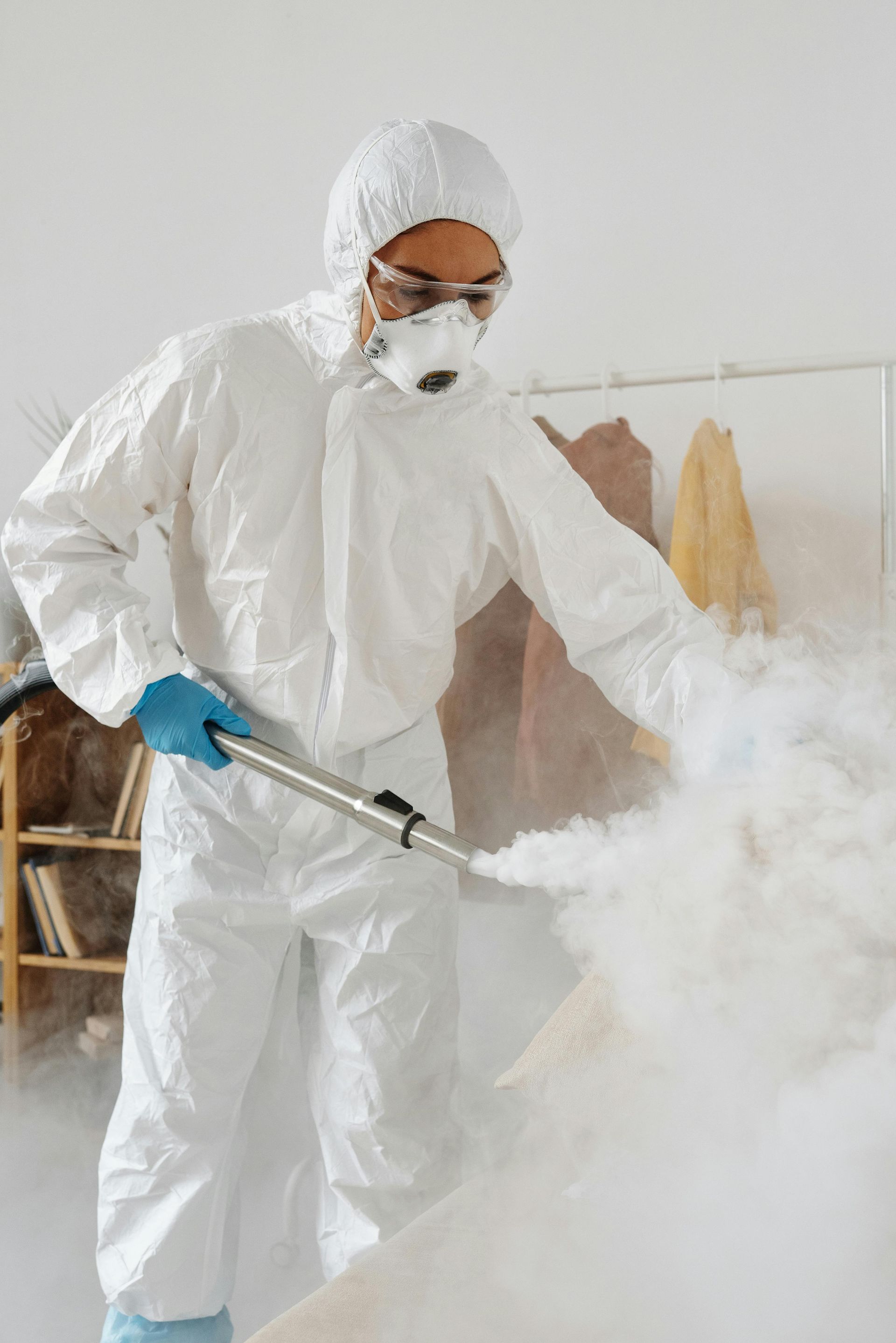 Person in hazmat suit sprays a cloudy mist; indoor setting.
