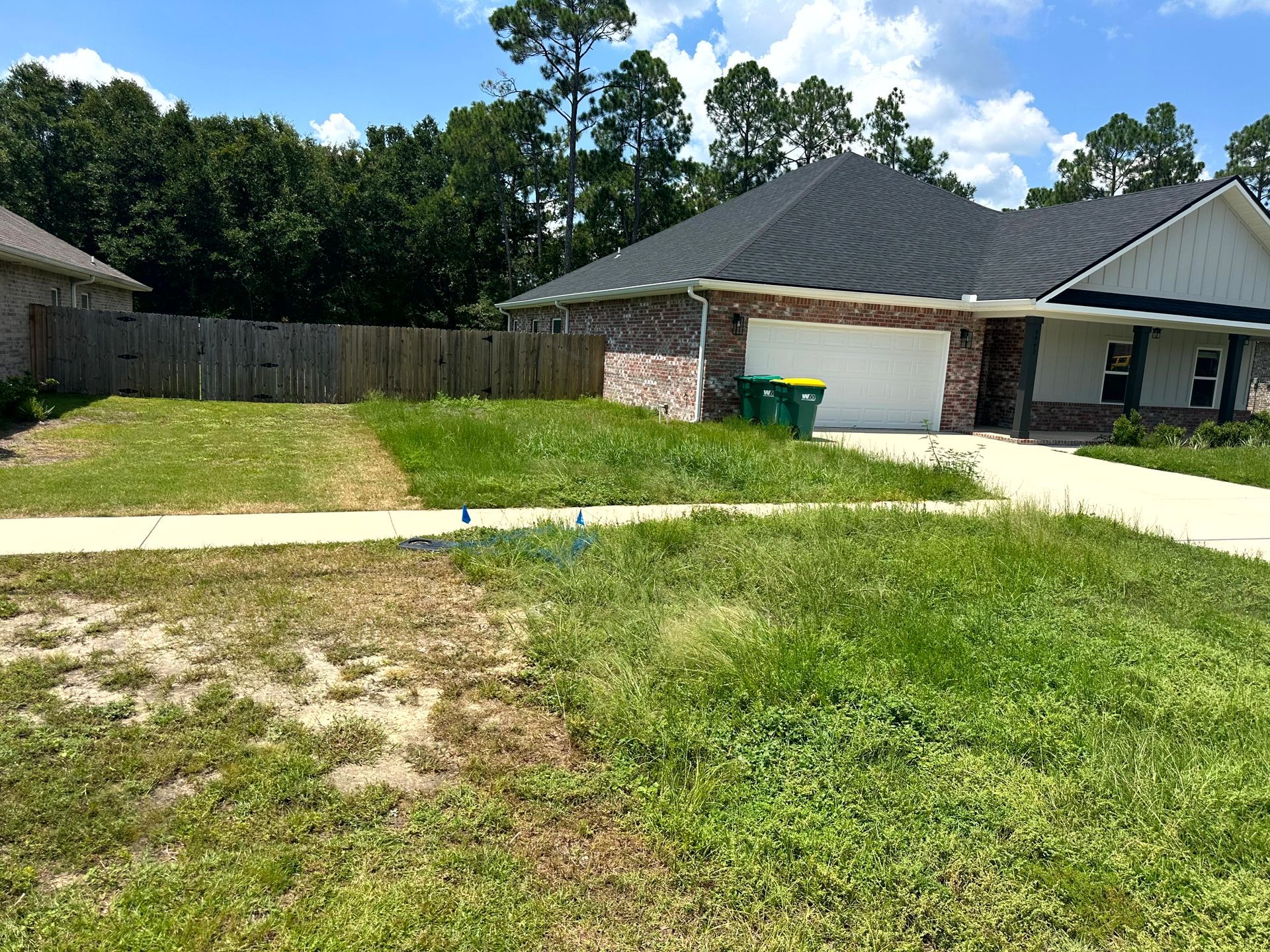 Lawn in front of a house. Green grass is overgrown. Brick home with a garage.