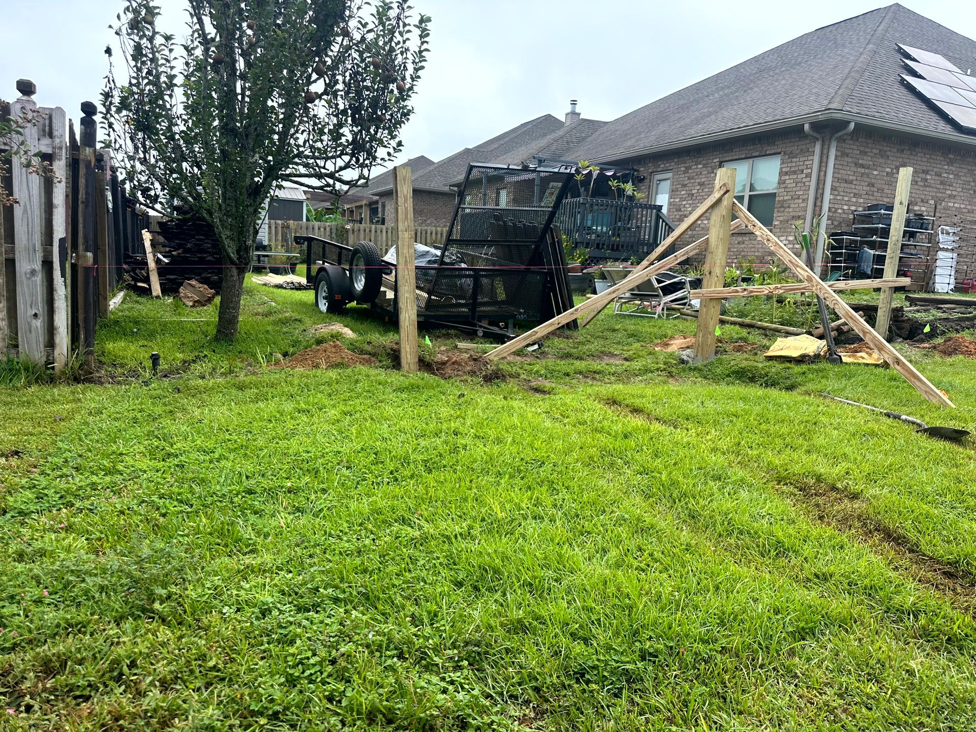 Backyard scene with a trailer, fence, and house under a cloudy sky. Green grass in the foreground.