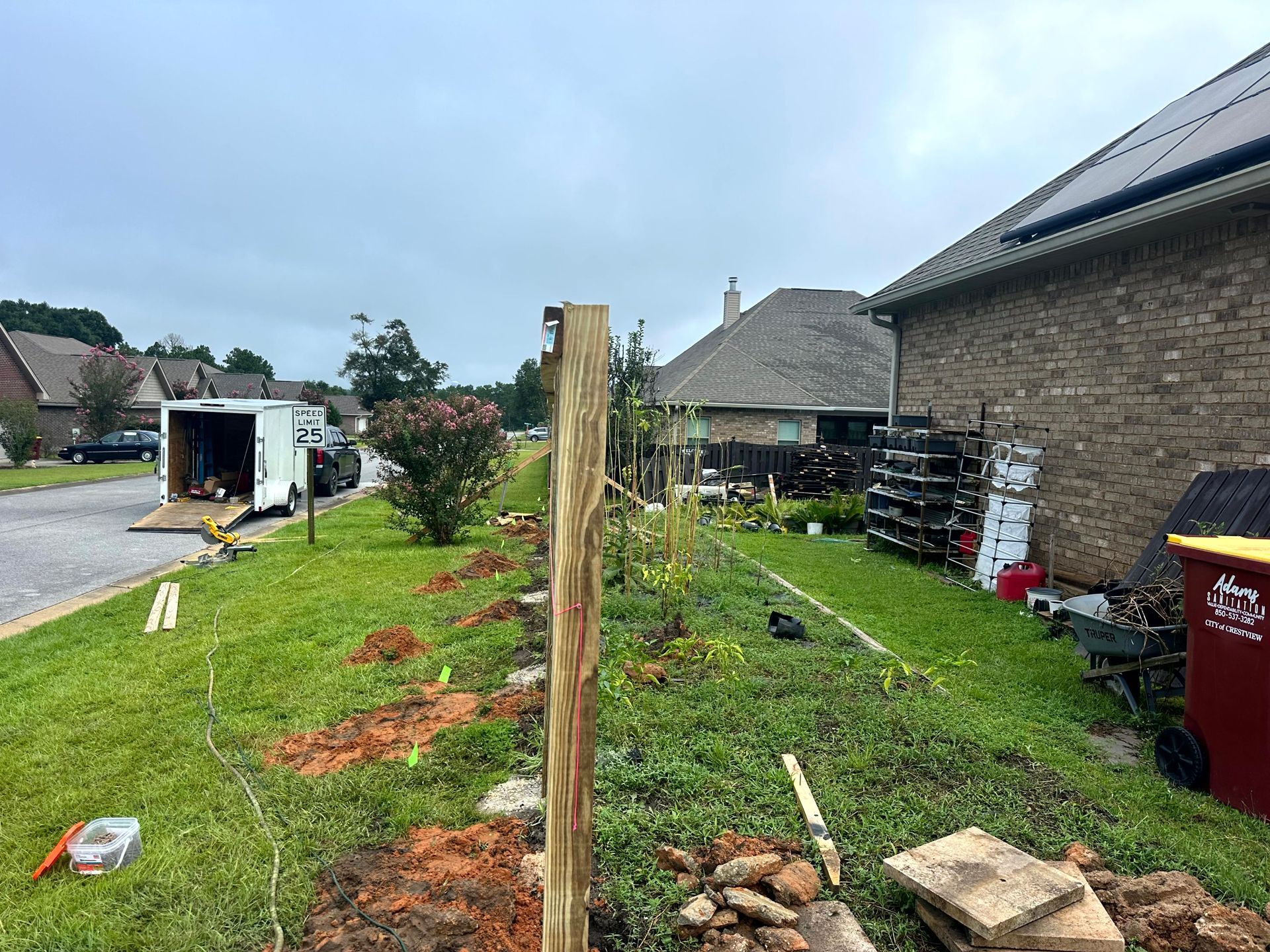Fence posts being installed in a grassy yard next to a street and house, overcast day.