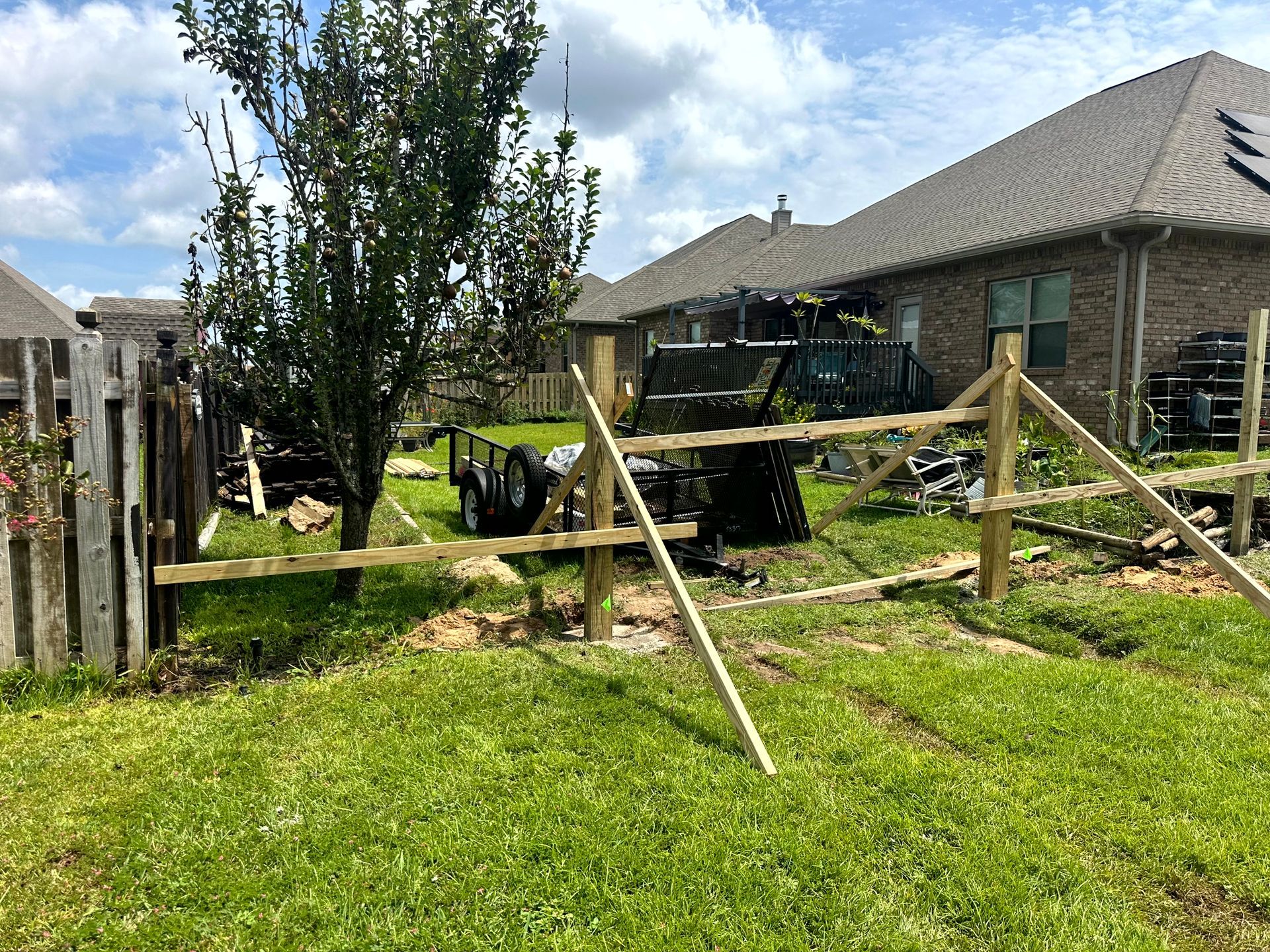 A split-rail fence under construction in a backyard with a trailer and a partially built wood fence.