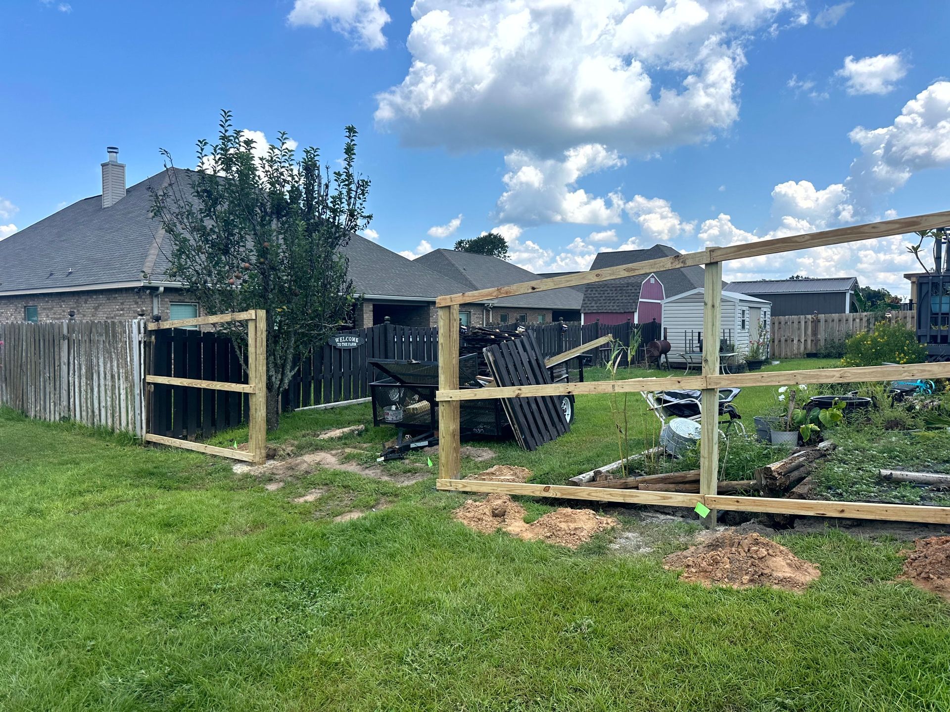 A partially constructed wooden fence in a backyard with a green lawn and blue sky.