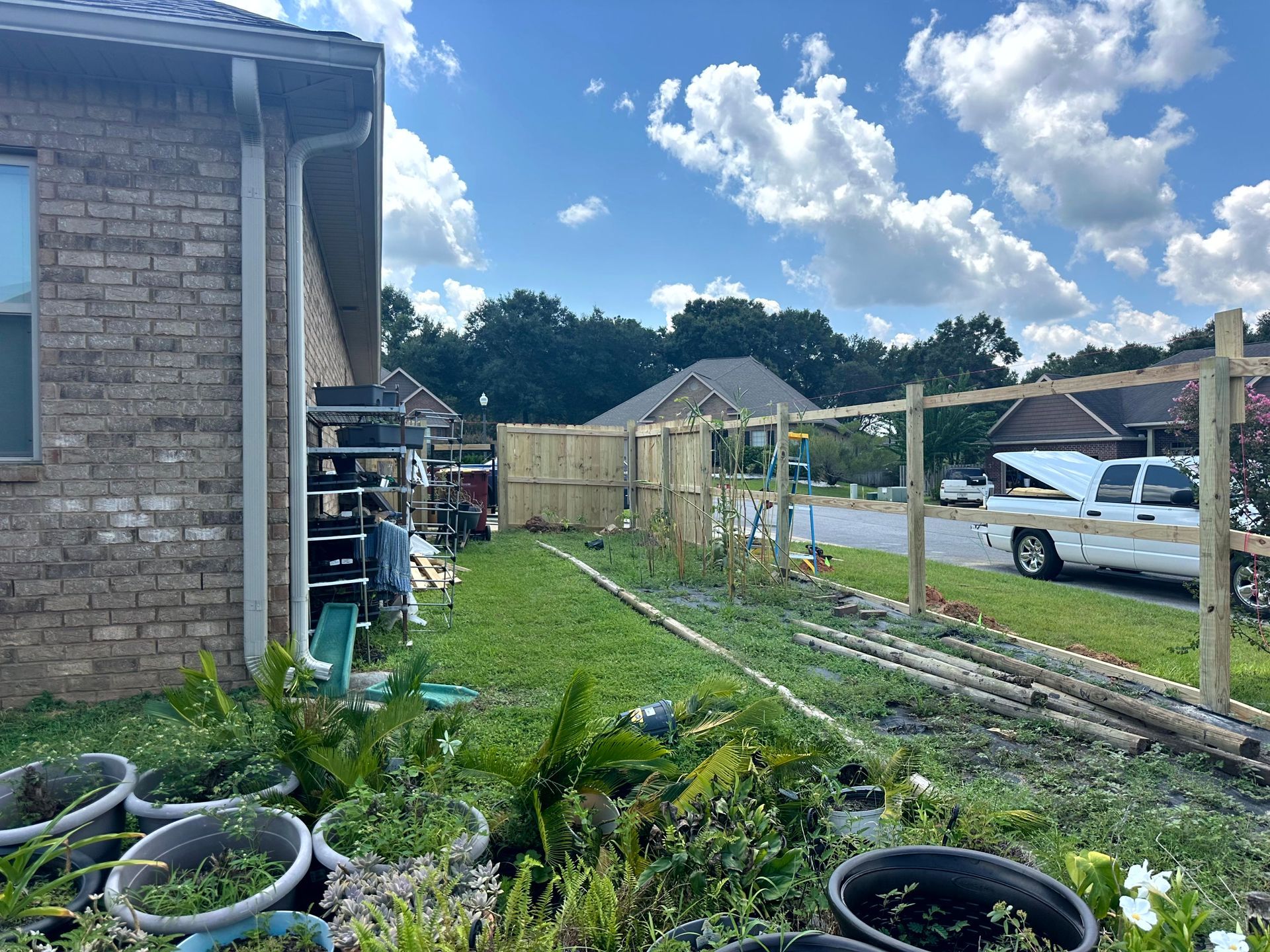 Backyard with a new wooden fence, potted plants, and a truck on a sunny day.
