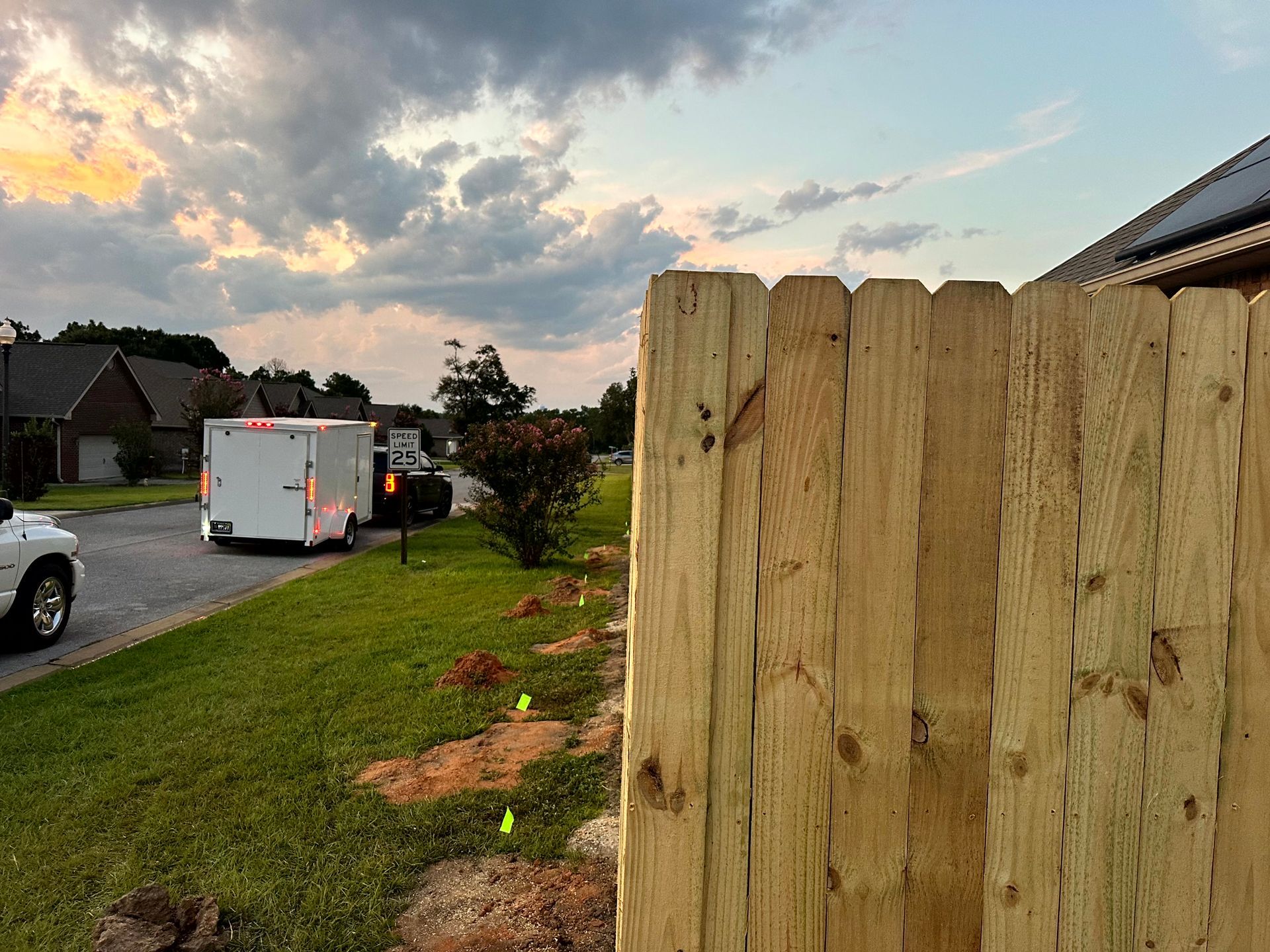 Wooden fence in foreground, street with trailer and sunset in background.