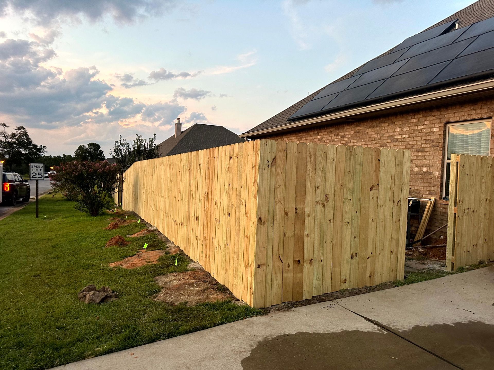 New wooden fence beside a brick house with solar panels, in a grassy yard.