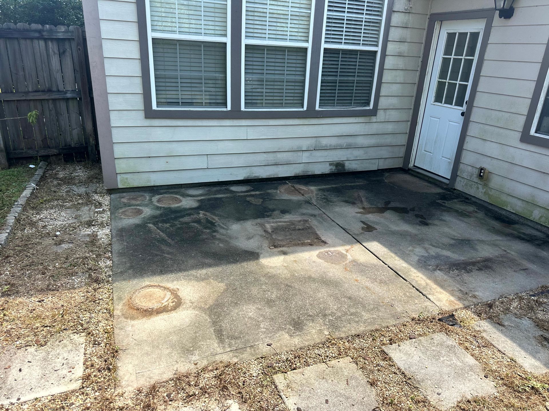 Concrete patio with dark stains, next to a house with windows and a door.