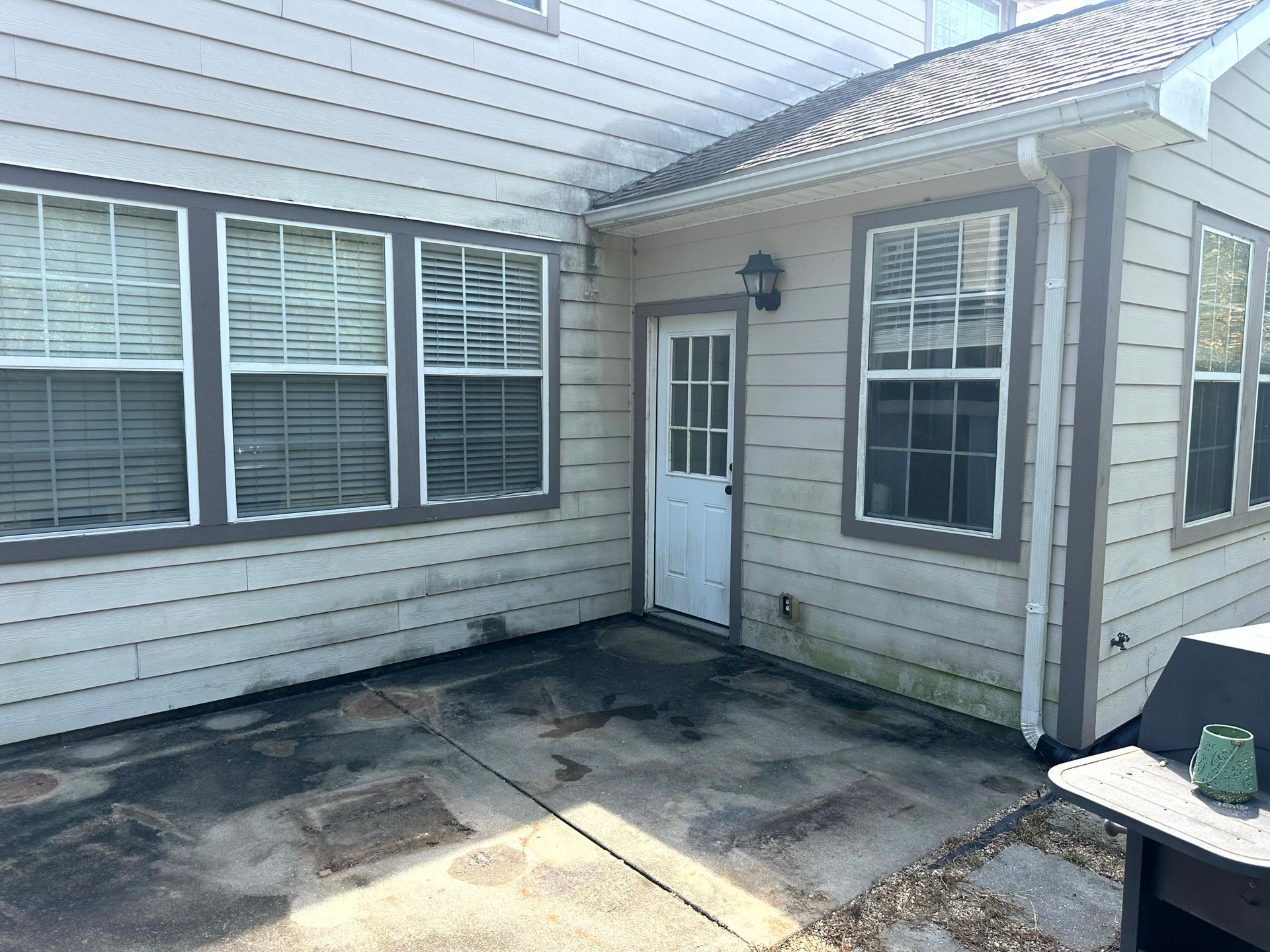 Patio with white siding, windows, and a door. The concrete has dark stains.