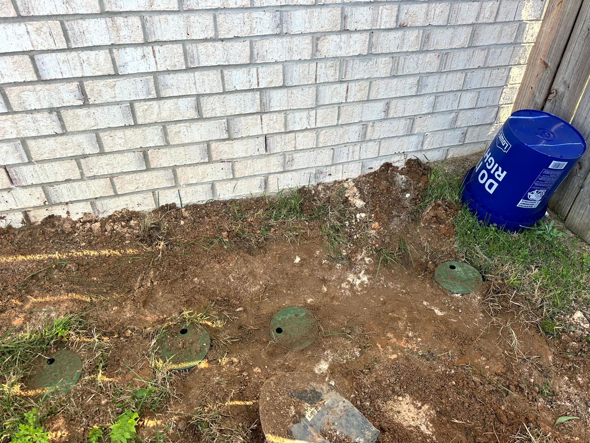 Dirt patch with brick wall, green sprinkler heads, and a blue bucket.