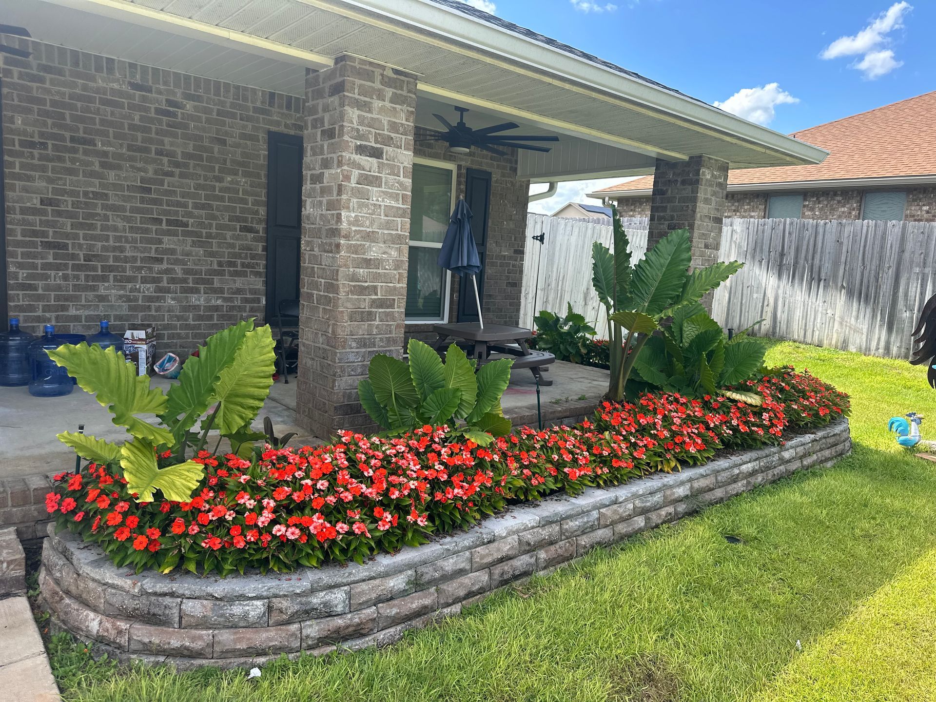 Brick home exterior with a garden bed of red flowers and large green plants.