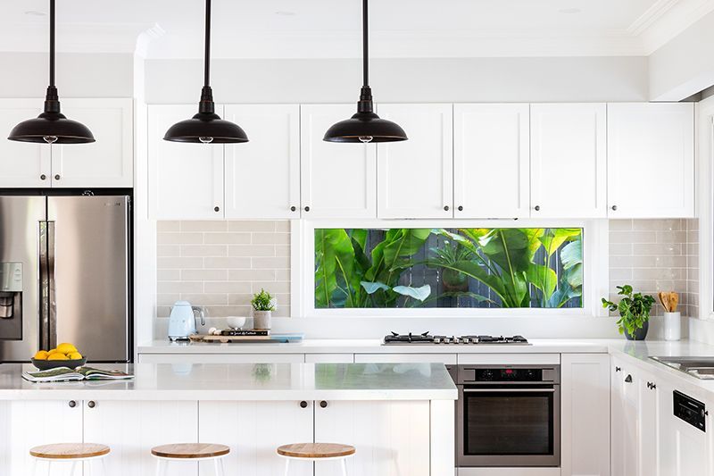 A kitchen with white cabinets , stainless steel appliances , a refrigerator and a window.