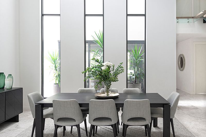 A dining room with a table and chairs and a vase of flowers on the table.