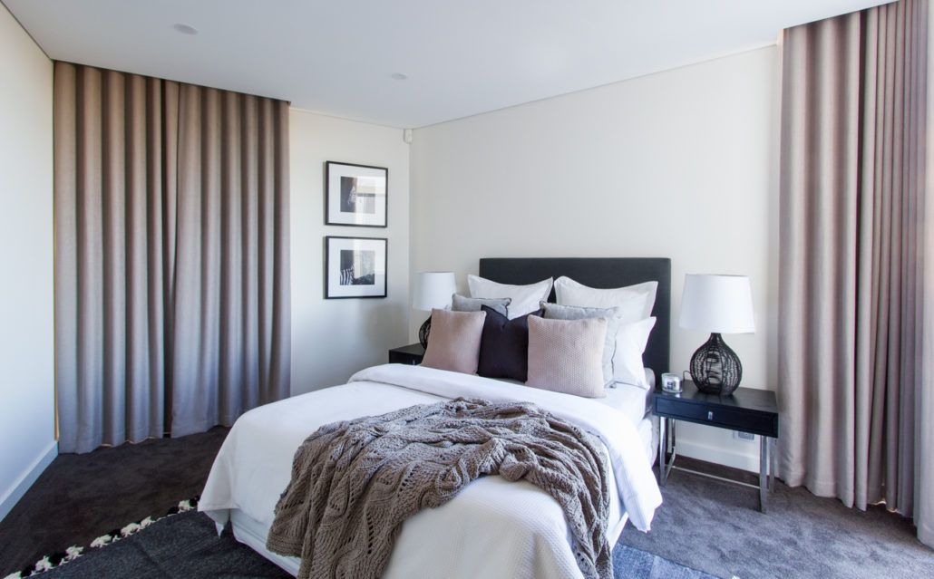 A bedroom with a bed , nightstand , lamps and curtains.