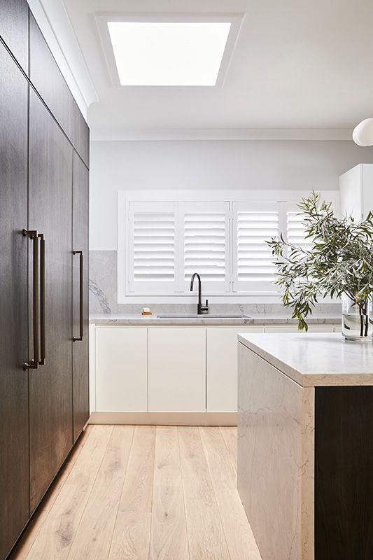 A kitchen with white cabinets , a sink , and a skylight.