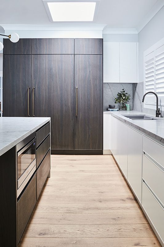 A kitchen with wooden floors , white cabinets , stainless steel appliances and a sink.