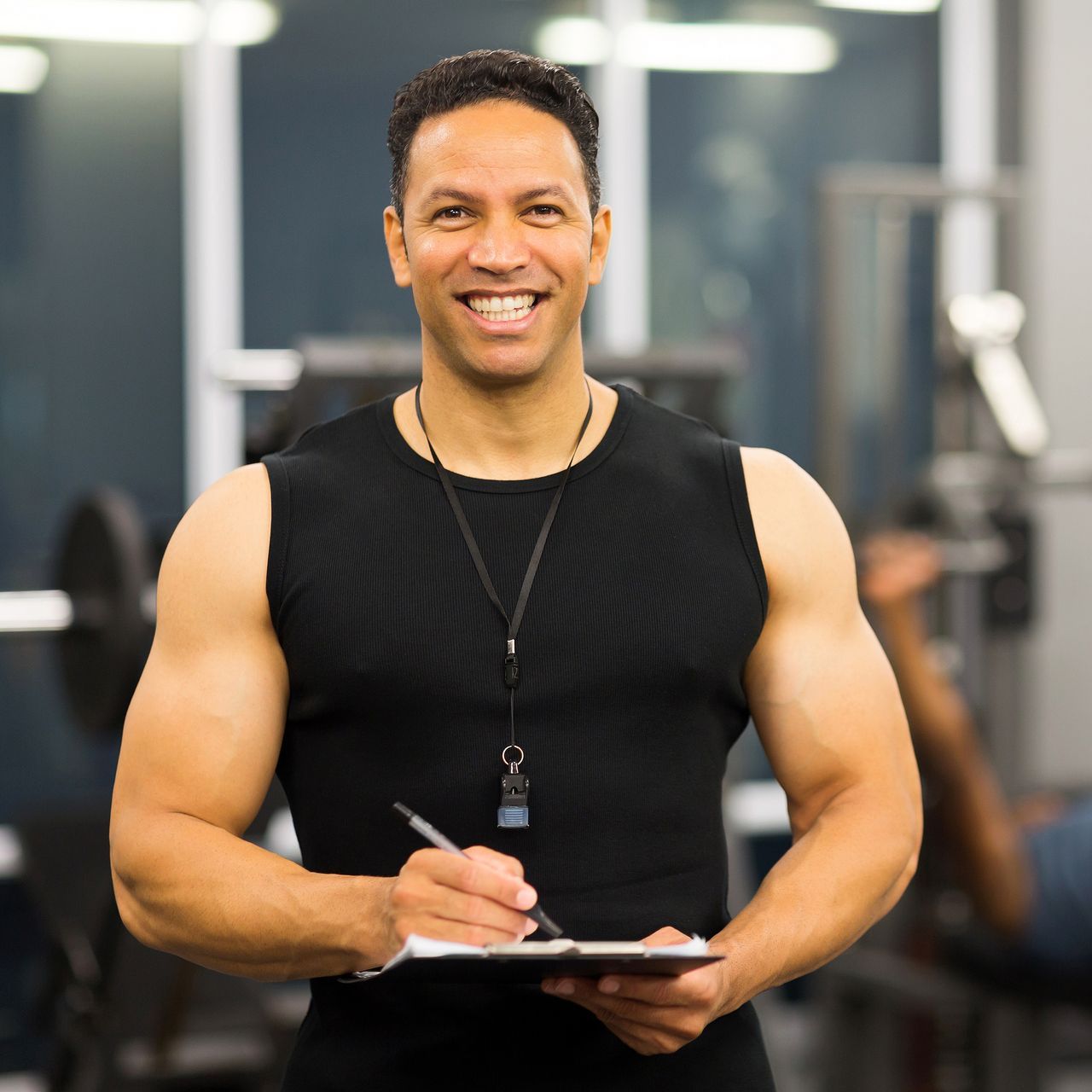 A man is holding a clipboard and smiling in a gym