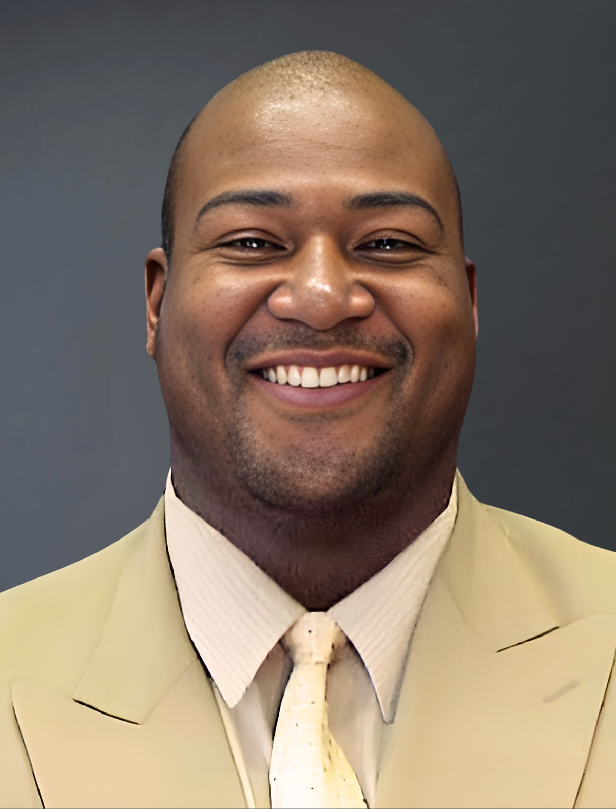 A man in a tan suit and tie smiles for the camera