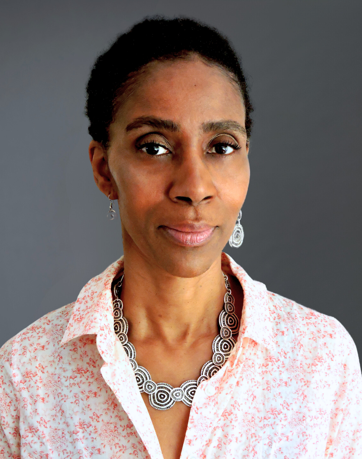 A woman wearing a necklace and earrings is looking at the camera.