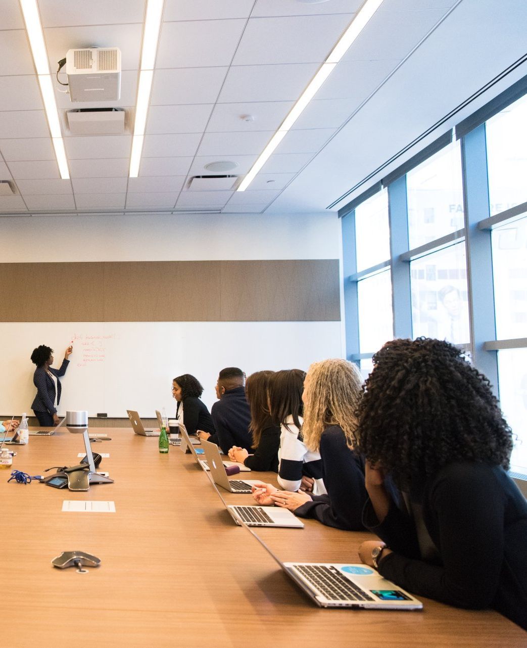 A group of people are sitting around a conference table with laptops.