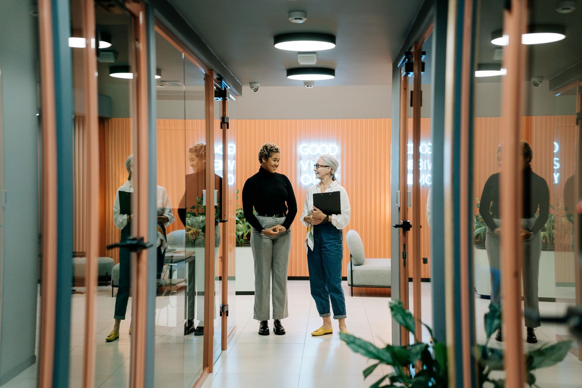 Two women are standing in a hallway talking to each other.