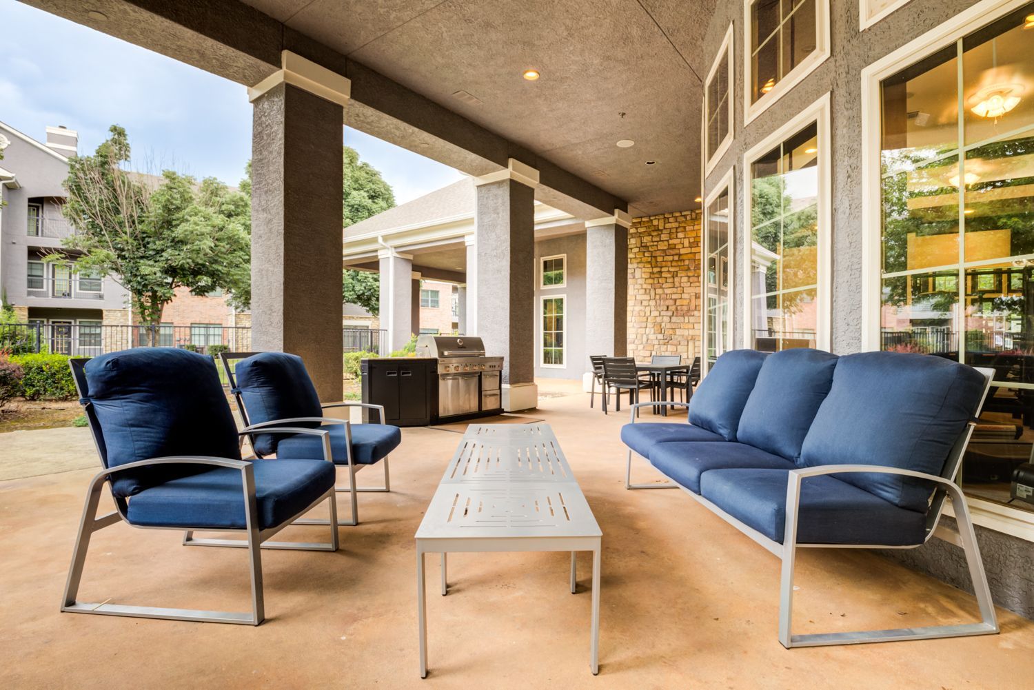 Outdoor patio with blue seating, grill, and stone wall.