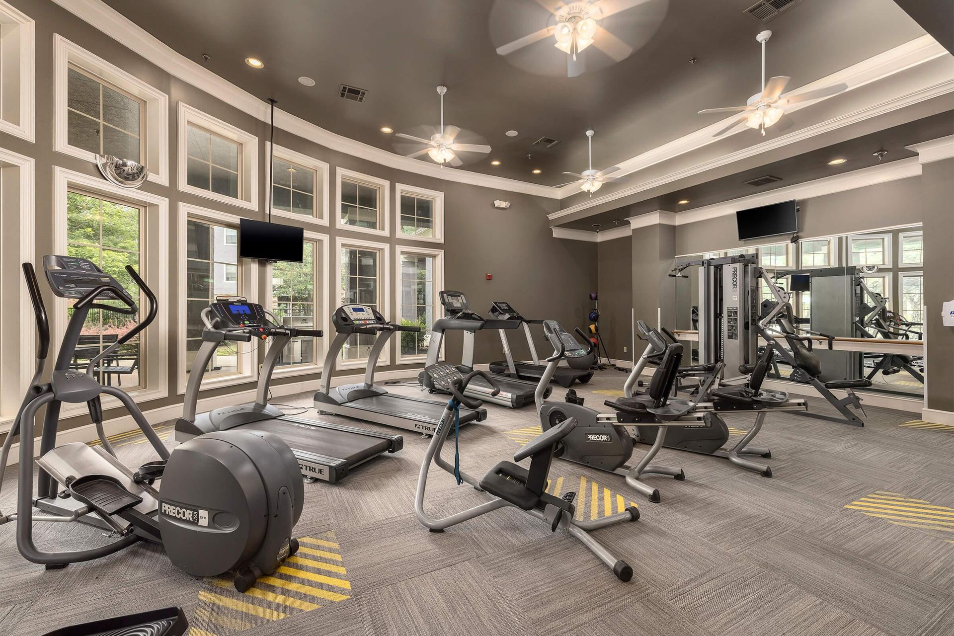 Gym with cardio machines, weight machines, natural light, and ceiling fans.