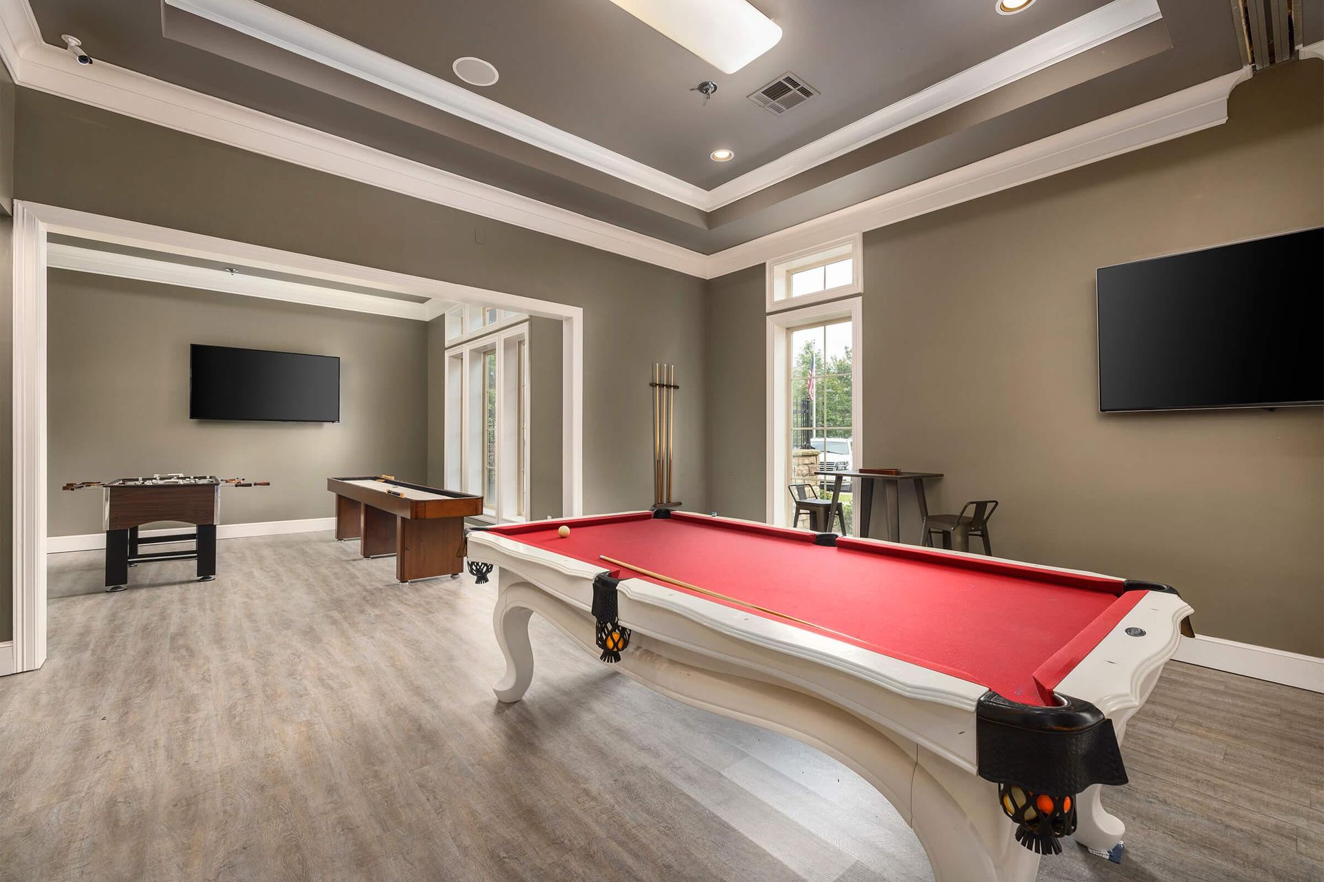 Game room with a pool table, foosball, and TVs. Features red felt and gray walls.