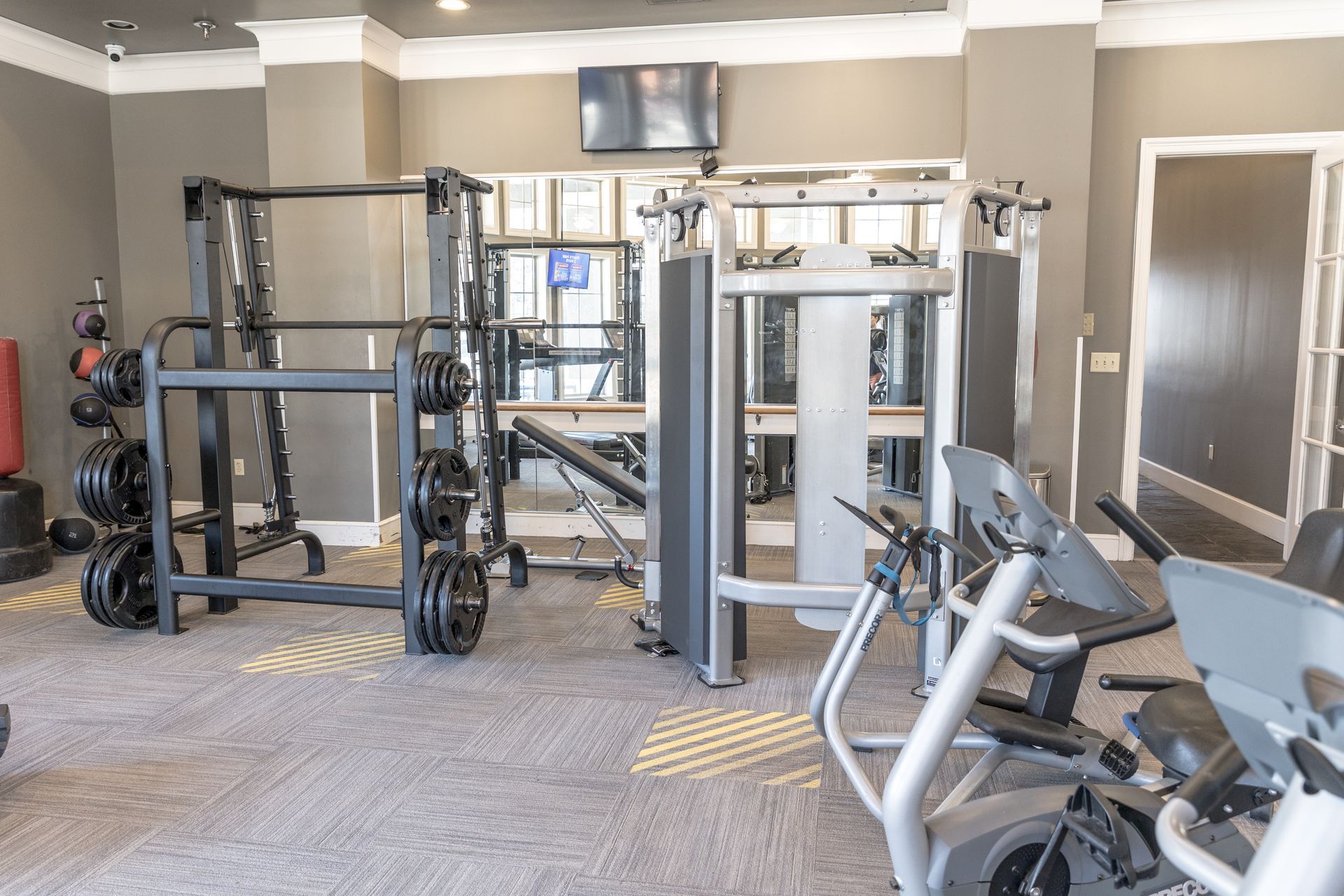Gym with weight machines, free weights, and cardio equipment. Gray walls and carpet.