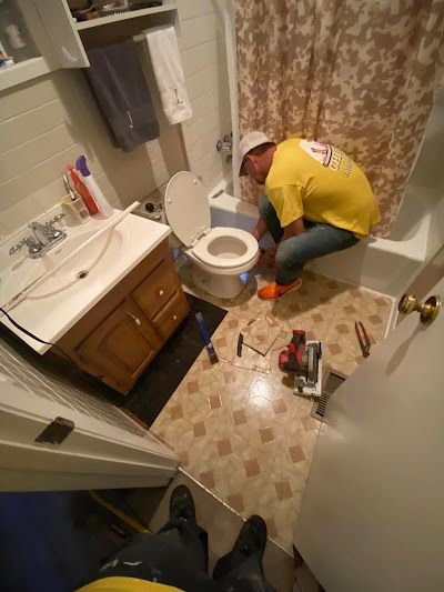 A plumber is fixing a sink in a kitchen with a drill.
