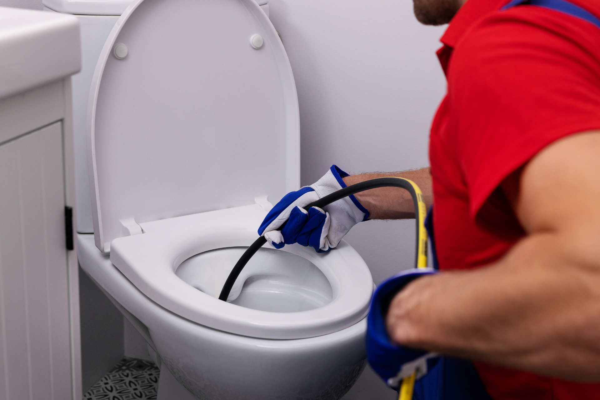A man is cleaning a toilet with a hose.